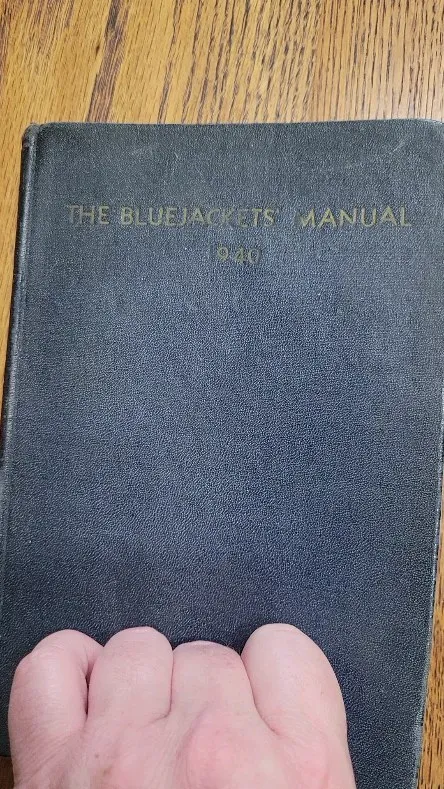 A worn 1940 copy of The Bluejackets' Manual held on a wood floor